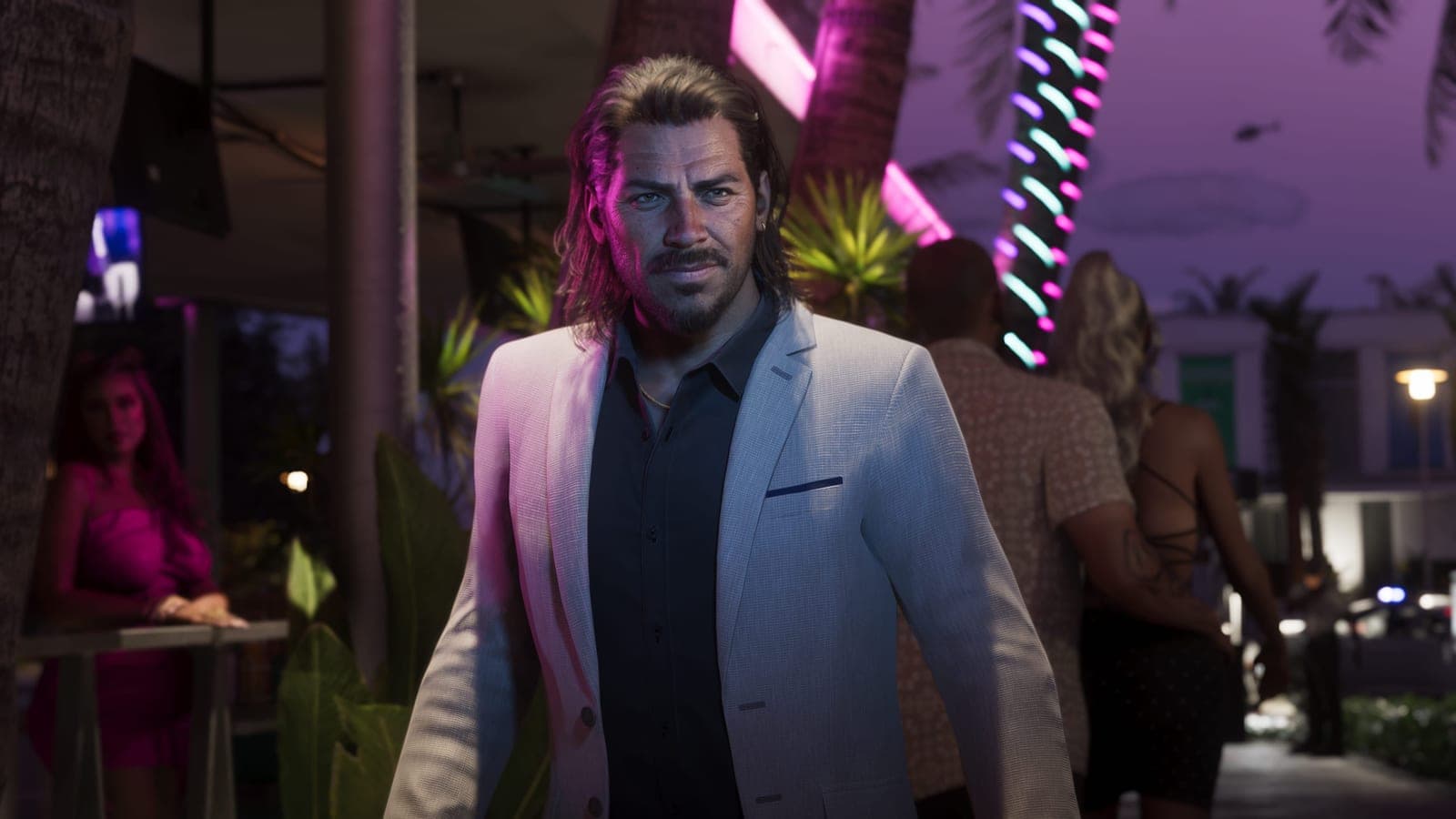 Raul Bautista in a pale suit and open black shirt, lit by neon palm lights on a Vice City street at night.