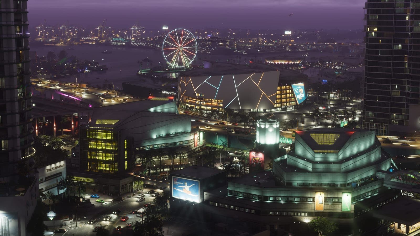 Downtown Vice City at night from the air, an arena and a ferris wheel lit up along the waterfront and port cranes in the distance.