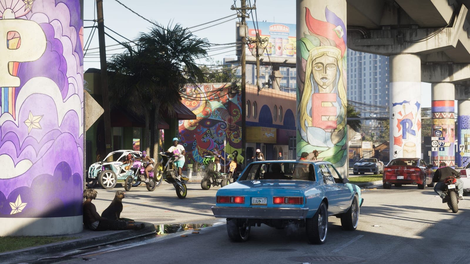A street under a concrete flyover in Vice City, its pillars painted with large murals, riders on dirt bikes and quad bikes crossing behind a pale blue saloon car.