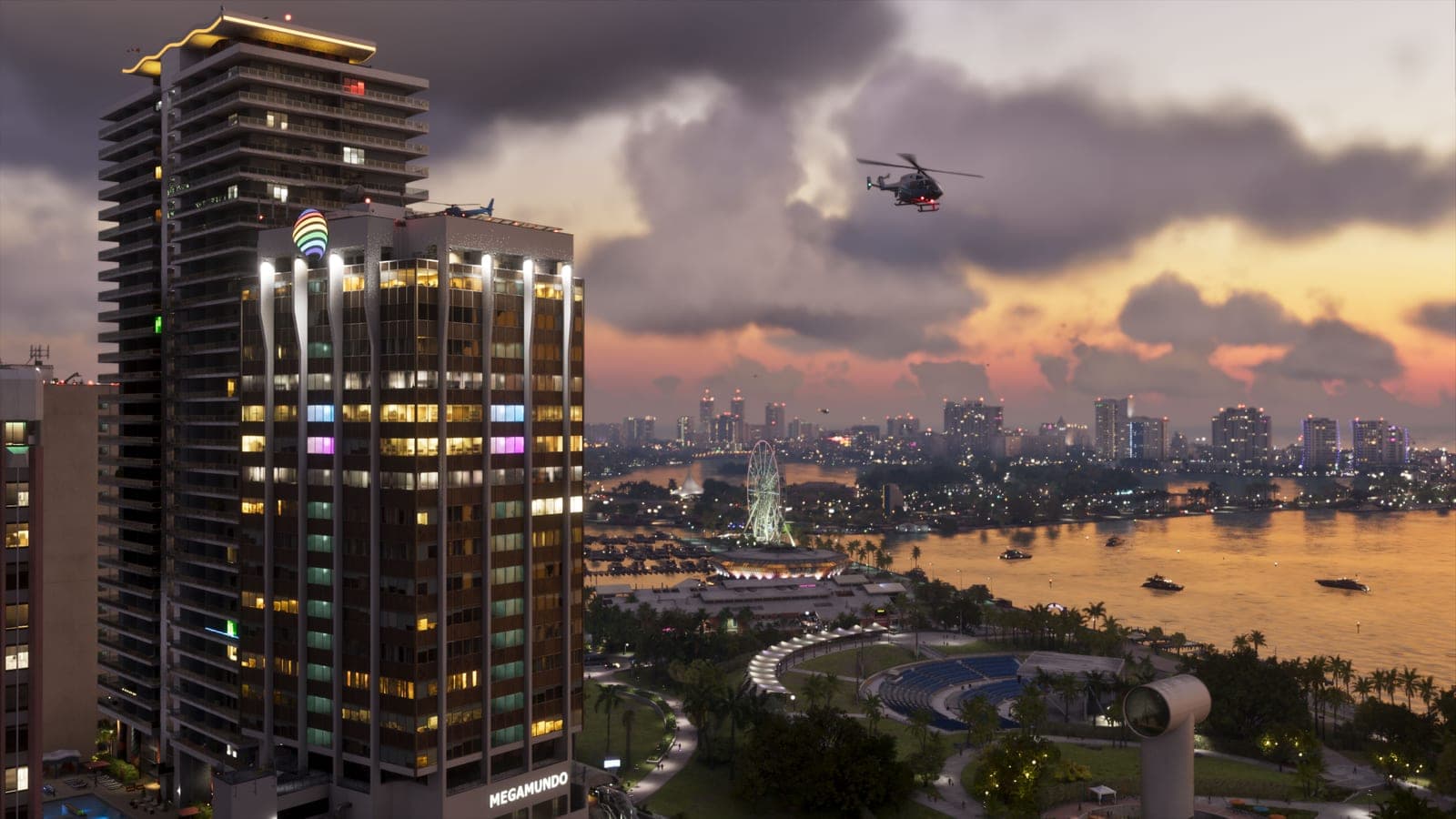 Vice City at sunset seen from above, a tower block lit with coloured window panels, a helicopter over the bay, and a ferris wheel and city lights along the far shore.